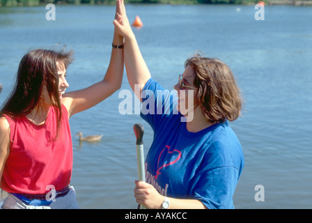 Canoeing racers age 34 at Lake Nokomis giving high five. Courage Center Canoe Race Fundraiser Minneapolis Minnesota USA Stock Photo