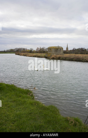 'River Thames' Lechlade Gloucestershire with white swans 'pill box' and 'St Lawrence Church' on a cold windy day Stock Photo