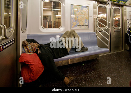 A homeless man sleeps on a subway seat in New York City Stock Photo