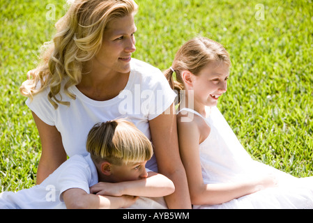 Mother sitting on grassy front lawn with her son and daughter Stock Photo