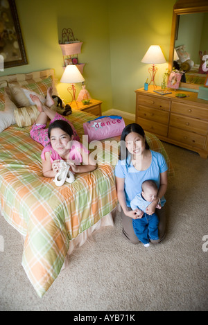Teenage girl lying on bed in bedroom with mom and baby brother Stock Photo