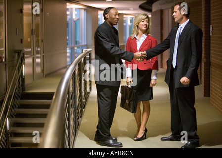 Side view of businesspeople standing in an office hallway and lobby shaking hands Stock Photo