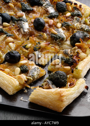 Close up of a pissaladiere pizza with black olives anchovies and pine nuts on black baking tray Stock Photo