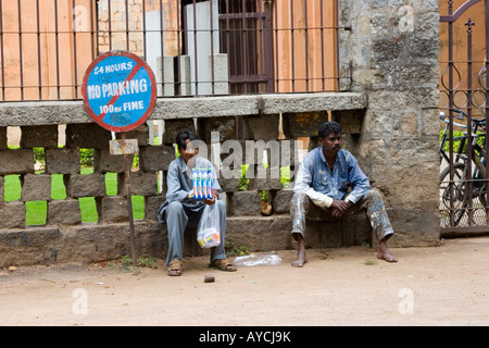 Two men sitting on the street next to a no parking sign Stock Photo