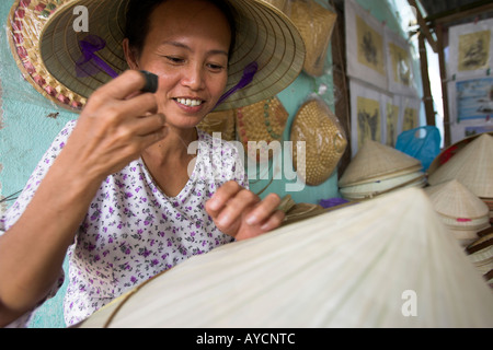 Woman stitches palm leaf sections on bamboo frame making conical hat Tu Duc village near Hue central Vietnam Stock Photo