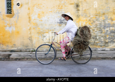 Conical hat woman rides loaded bicycle from market Hoi An historic town mid Vietnam Stock Photo