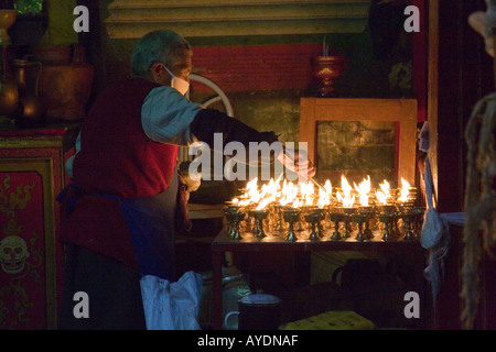 Tibetan monk tending yak butter candles on a shrine in a small monastary located in Lhasa Tibet Stock Photo