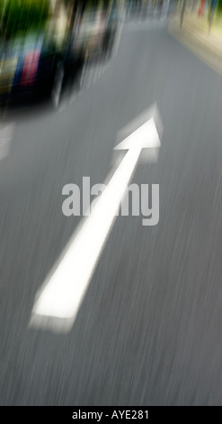 PORTRAIT SHOT OF WHITE ARROW ON TARMAC ROAD SHOWING DIRECTION WITH BLURRED BACKGROUND Stock Photo