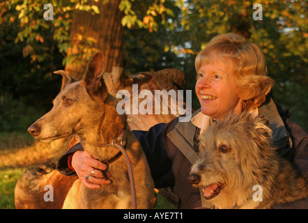 Female with two Lurcher dogs sitting in woods Stock Photo