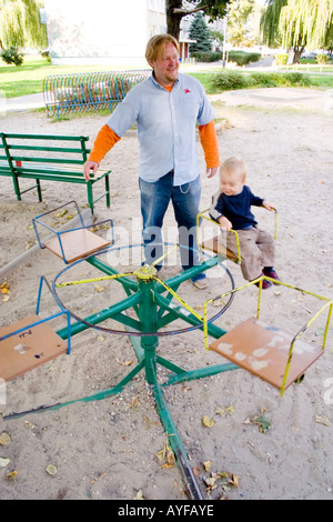 Toddler having a wonderful time on antiquated self-propelled merry-go-round with dad age 32. Lodz Central Poland Stock Photo