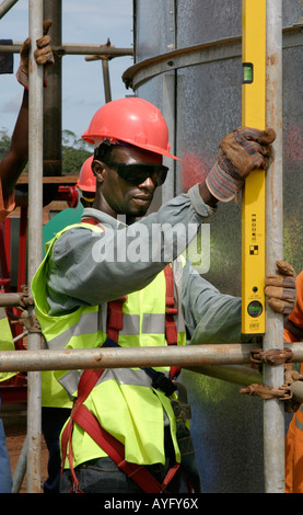 Construction worker using spirit level while putting up scaffolding for water and sewage treatment plant,Ghana, West Africa Stock Photo