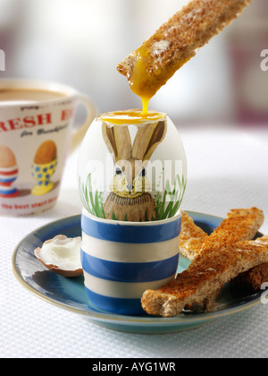 Traditional hand painted decorated boiled easter rabbit egg in a breakfast setting with toast being dipped into the egg Stock Photo