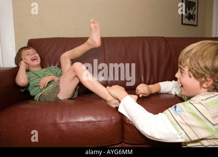 older brother tickling five year old younger brother at home on sofa Stock Photo