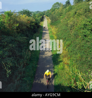 Looking along Tarka Trail with two people cycling one at speed blurred yellow with white helmet Braunton North Devon England Stock Photo