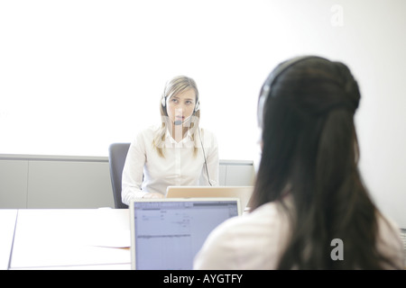 Two businesswomen wearing headsets and working with laptops in office Stock Photo