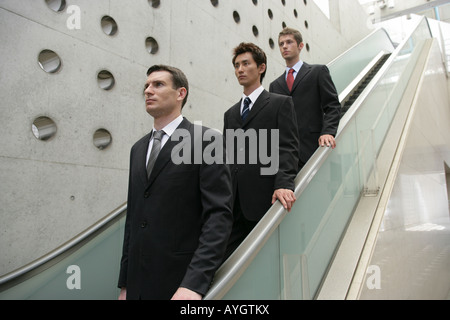 Three business men going down escalator Stock Photo