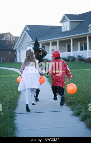 Children in Halloween costumes skipping on sidewalk Stock Photo