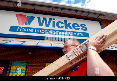 A tubby male assistant at a Wickes DIY store carries planks of wood Stock Photo
