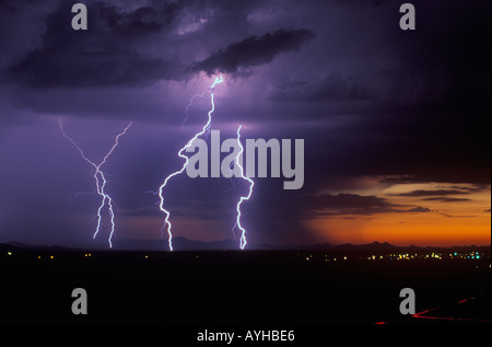 Large lightning bolts striking at sunset with city lights during a summer monsoon storm in Marana, Arizona, United States. Stock Photo