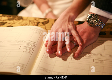Newly married couple husband and wife holding hands on top of civil marriage register book during a UK civil wedding ceremony Stock Photo
