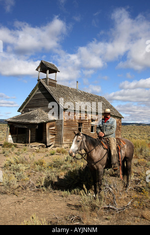 Cowboy on Quarter Horse (Equus caballus) standing next to a ruin of an old school which is built in 1900 Stock Photo