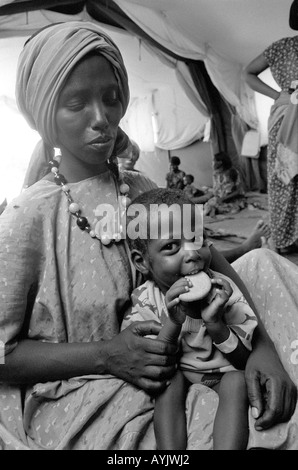 B/W of a Somali woman with her malnourished child eating a protein biscuit at an emergency feeding centre at a refugee camp. Kebrebeyah, Ethiopia Stock Photo