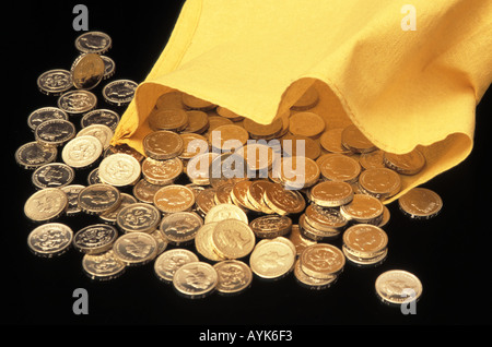 Close up pile of British UK currency in one pound sterling cash coins spilling out pounds of loose change from yellow bank money bag Stock Photo