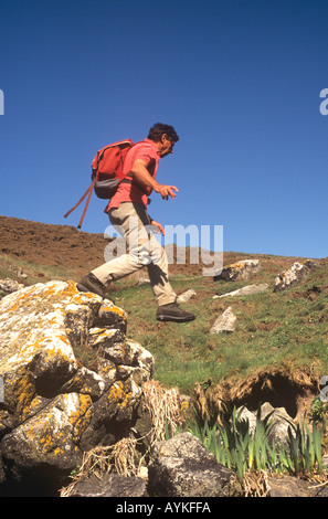 Retired man scrambling and jumping over rocks in Cornwall, UK Stock Photo