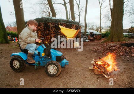 Boy playing with a toy excavator next to a fire Stock Photo