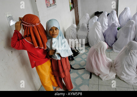 Two young muslim girls in Banda Aceh Indonesia are playing while the older girls pray Stock Photo