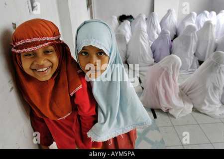 Two young muslim girls in Banda Aceh Indonesia are playing while the older girls pray Stock Photo