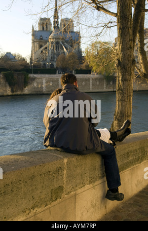 Lovers embracing along the Seine River in Paris with Notre Dame Cathedral in the background. Stock Photo