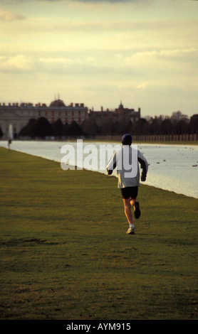 Jogger running along The Long Water towards Hampton Court Palace in the late afternoon in winter Stock Photo