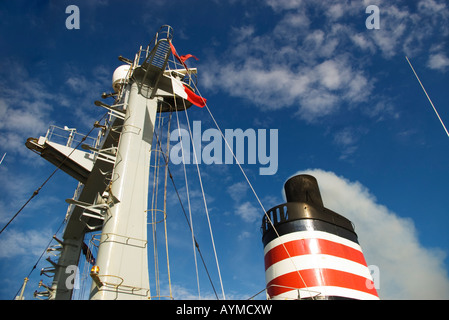A ship's funnel and mast with smoke  coming from the funnel. The flag indicates the ship has a pilot on board. Stock Photo