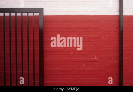 Detail of freshly painted cream and red brickwall with newly painted black metal security gate open against it and drainpipe Stock Photo