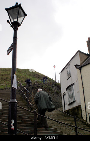 Mature man walking up steps towards Whitby Abbey with old gas lamp in view Whitby North Yorkshire Stock Photo