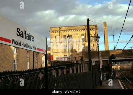 Saltaire World Heritage Site Sign stating above on Saltaire Station with mill and chimney in background Stock Photo