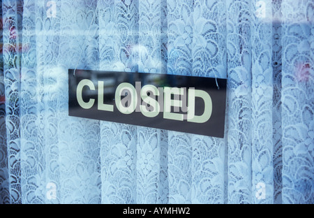 Black and white sign in a shop or kiosk or cafe window with fancy net curtains and reflections stating Closed Stock Photo