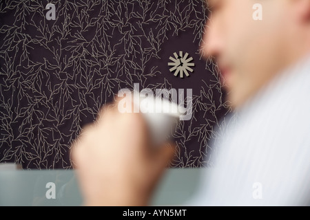 Businessman holding a cup of coffee, a wall clock in the background Stock Photo