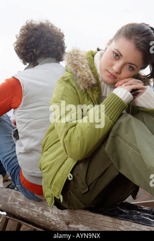 Young woman and man with curly hair sitting back to back in a winterly landscape Stock Photo