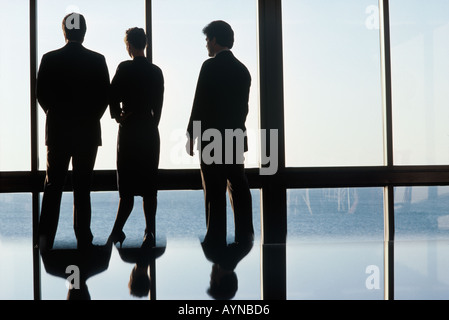 Silhouette of three professional business people looking out a large window with reflection on the conference table Stock Photo