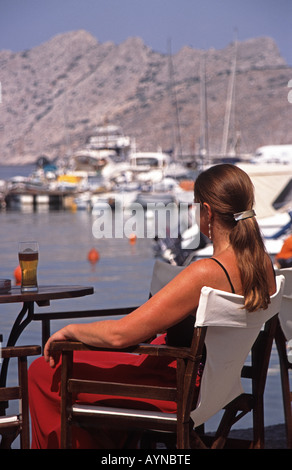 AEGINA, GREECE. A woman sitting at a bar by the harbour in the village of Perdika. Stock Photo
