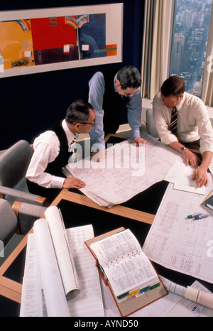Overhead view of Asian American and Caucasian engineers in their office meeting and reviewing blueprints Stock Photo