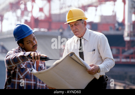 Caucasian engineer African American foreman reviewing blueprints on construction site Stock Photo