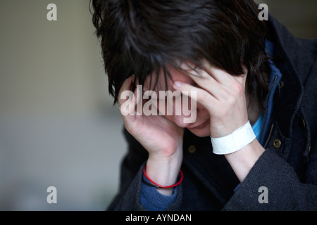 young dark haired teenage man sitting with his head in his hands staring at the floor Stock Photo
