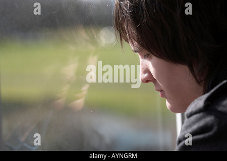 young dark haired teenage man staring out through a dirty window with reflection Stock Photo