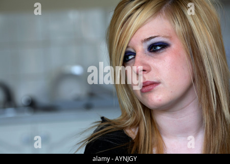 teenage blonde haired woman sitting crying in her kitchen bedsit Stock Photo