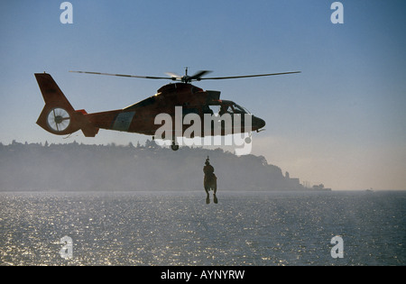 A United States Coast Guard helicopter raises a Rescue Swimmer and a shipwreck victim from an overturned boat in the Seattle Harbor. Stock Photo
