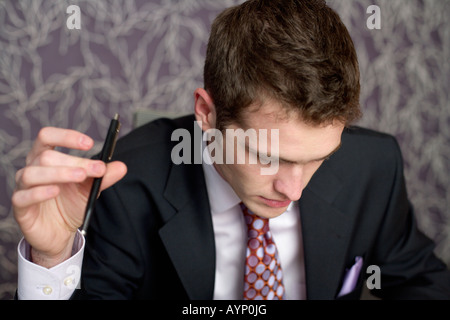 Businessman sitting at his desktop, holding a pen Stock Photo