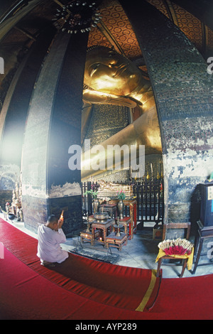 Buddhist monk burning prayer incense under Reclining Buddha at Wat Po in Bangkok Stock Photo